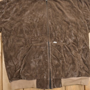 May include: A brown suede zip-up jacket with a kangaroo pocket and a brown ribbed knit waistband.