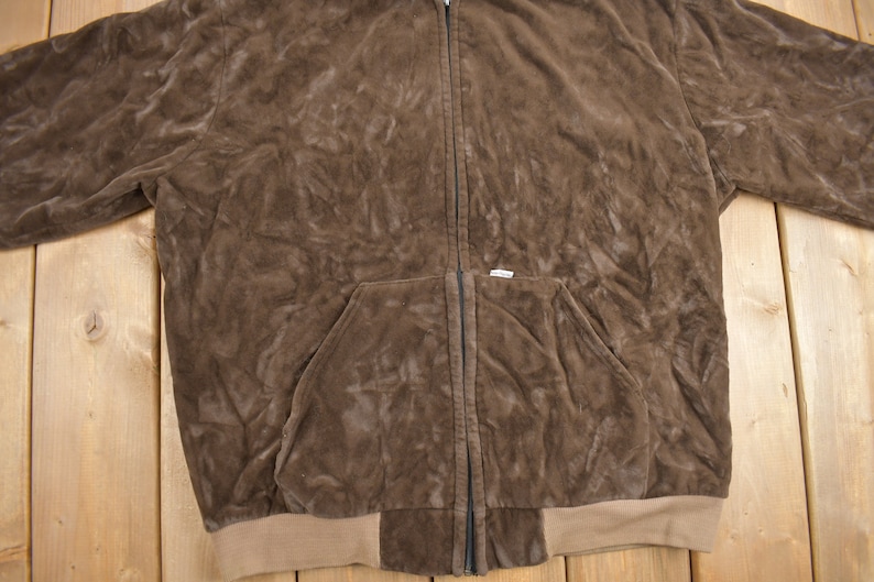 May include: A brown suede zip-up jacket with a kangaroo pocket and a brown ribbed knit waistband.