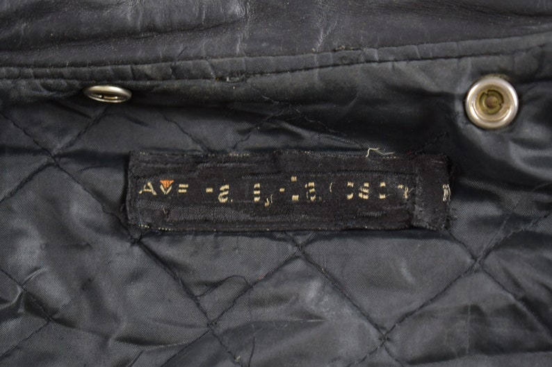 Puede incluir: Primer plano del forro de una chaqueta de cuero negra con una etiqueta negra que dice "AV = -2. = -2. 55CT".