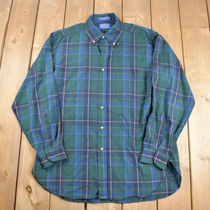 May include: A long-sleeved plaid shirt in green, blue, and brown. The shirt has a button-down collar and a button-up front.