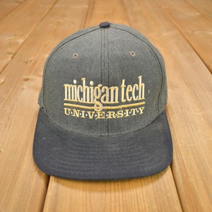 Puede incluir: Una gorra de béisbol gris oscuro y negra con el texto bordado "michigan tech UNIVERSITY" en dorado.