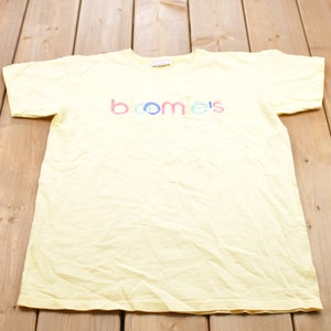 May include: A yellow t-shirt with the word "boomers" printed on the front in rainbow colors.