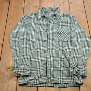 May include: A green and white plaid long-sleeved button-up shirt with a pocket on the left side.