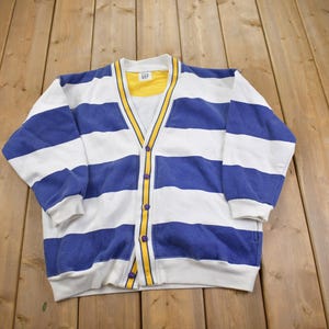 May include: A white and blue striped cardigan with a yellow button closure. The cardigan has a V-neck and long sleeves.