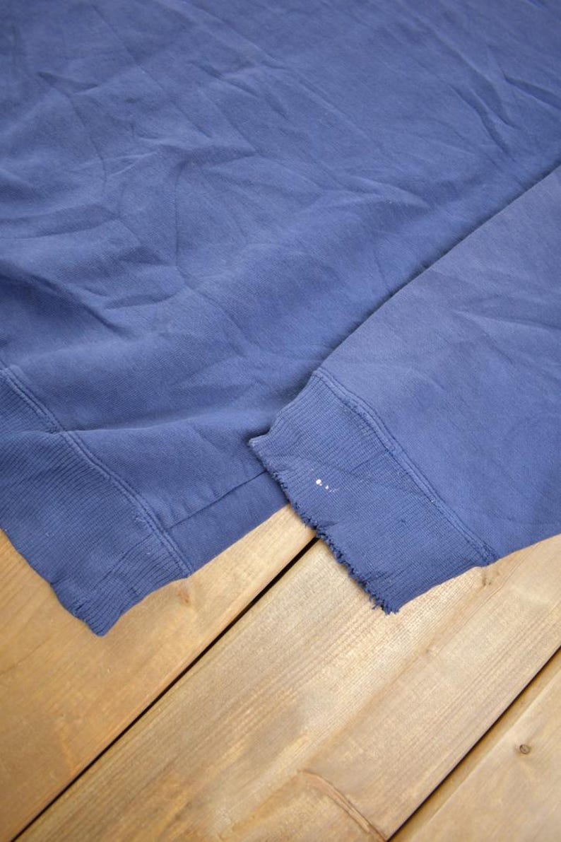 May include: A blue sweatshirt with a frayed edge on the sleeve.