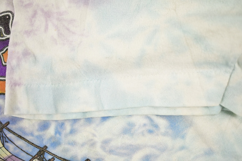 May include: Close-up of a light blue tie-dye t-shirt with a white seam along the bottom edge.