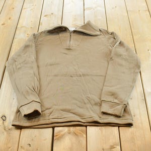 Peut inclure: Un sweat-shirt à manches longues de couleur beige doté d'une fermeture éclair métallique d'un quart de longueur au centre du col. Le vêtement présente un col rabattu, des poignets côtelés au bout de chaque manche et un ourlet droit.