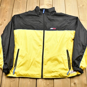Pu&ograve; includere: Una giacca a vento nera e gialla con una cerniera blu e un piccolo logo sul petto.