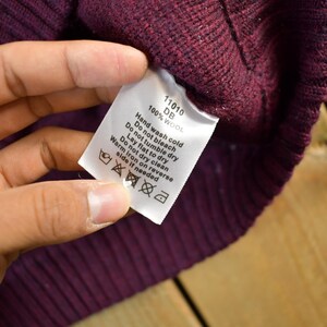 Puede incluir: Primer plano de un su&eacute;ter de lana burdeos con una etiqueta blanca. La etiqueta muestra las instrucciones de cuidado: lavar a mano con agua fr&iacute;a, no usar secadora, secar en plano, no limpiar en seco, planchar del rev&eacute;s con plancha tibia.