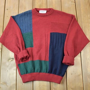 Może przedstawiać: Czerwony sweter w niebiesko-zielono-białe wzory z okrągłym dekoltem. Sweter ma metkę z napisem "Made in Italy".