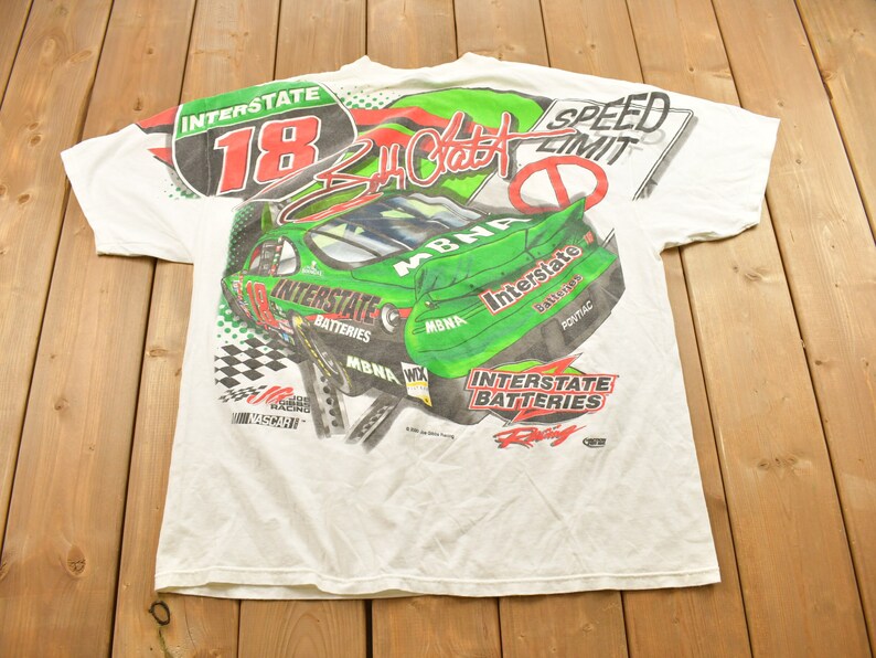 May include: White t-shirt with a green and red print of a racing car with the number 18 and the text "Interstate Batteries" and "Speed Limit".