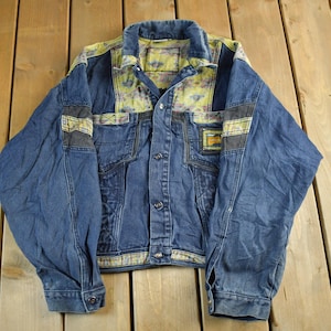 May include: A vintage blue denim jacket with a unique design. The jacket features a patterned collar and shoulder accents in yellow and green. It has button closures and pockets, offering a classic, retro style.