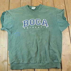 May include: Green sweatshirt with a blue and white "BOCA AUTHENTIC" logo printed on the front.