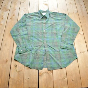 May include: A long-sleeved plaid shirt in shades of green and blue. The shirt has a button-down collar and a single pocket on the left chest.