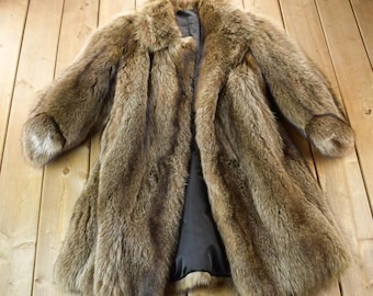May include: A long, brown fur coat with a dark lining. The coat has a classic collar and long sleeves. The fur appears to be thick and luxurious, with variations in color from light to dark brown.