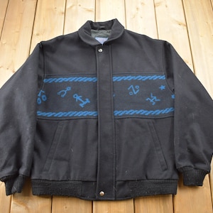 May include: A black wool bomber jacket with a blue and white patterned design. The pattern features nautical symbols such as anchors and ropes.