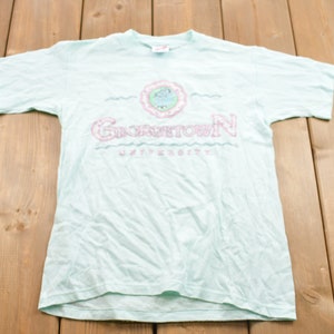 May include: A light blue t-shirt with a pink graphic of a wave and the text "GEORGETOWN UNIVERSITY".