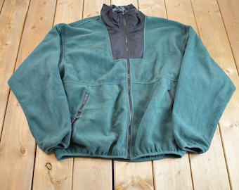 Puede incluir: Una chaqueta de forro polar verde oscuro con una cremallera negra y un panel negro en la parte superior de la espalda. La chaqueta tiene dos bolsillos con cremallera en la parte delantera.