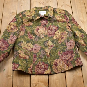 May include: A green, brown and pink floral patterned button-up jacket. The jacket has long sleeves and a collared neckline.