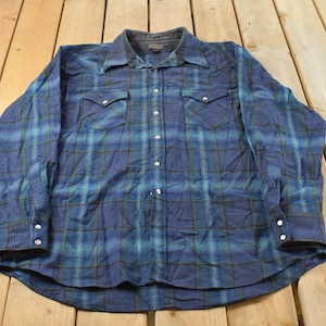 May include: Blue and green plaid button-down shirt with two chest pockets and snap closures. The long-sleeved shirt has a dark collar and cuffs. The shirt is made of a soft, comfortable material.