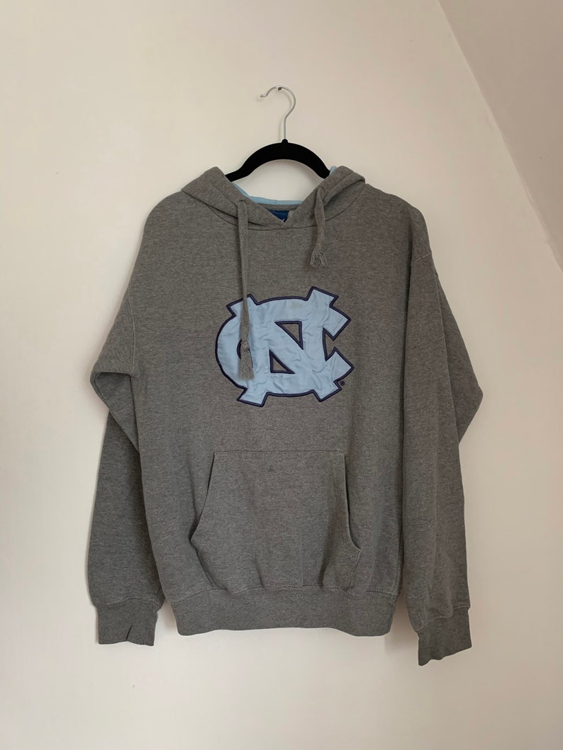 May include: Gray hooded sweatshirt with a blue and white North Carolina Tar Heels logo on the front.