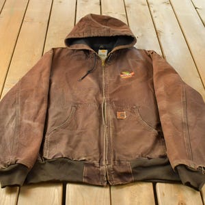 Peut inclure: Une veste à capuche zippée marron avec un ourlet et des poignets côtelés marron foncé, une doublure intérieure noire et un petit écusson logo sur la poitrine gauche. La veste possède deux poches avant et une fermeture éclair métallique.