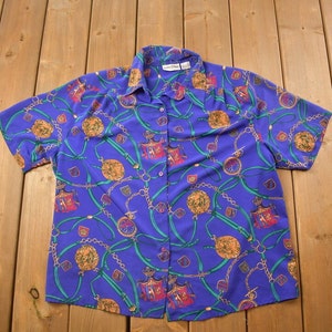 May include: A purple short-sleeved button-up shirt with a colourful pattern of chains, shields, and crowns.