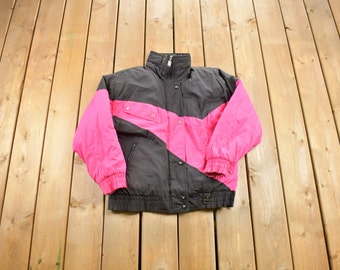 Könnte beinhalten: Eine schwarze und pinkfarbene Skijacke mit Reißverschluss und einem diagonalen pinkfarbenen Panel auf der Vorderseite.