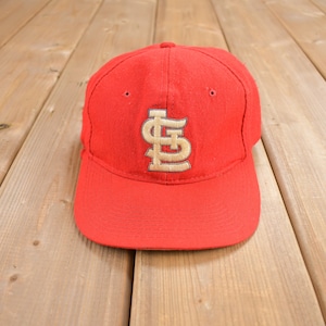 May include: A red baseball cap with a gold embroidered "St. Louis Cardinals" logo.