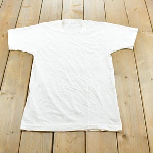 May include: A plain white short-sleeved t-shirt with a crew neckline. The garment features a simple, solid-colored design with a standard fit, short sleeves, and a straight hemline, presented in a clean, minimalist style without any patterns or prints.