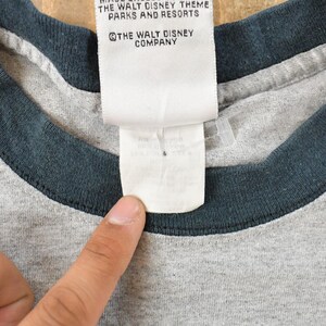 May include: Close-up of a gray t-shirt with a dark blue collar. A white tag with text from The Walt Disney Company is visible. The shirt is made of a soft, comfortable material.