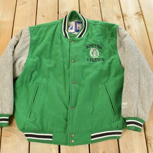 Può includere: Giacca college verde e grigia dei Boston Celtics. La giacca ha un corpo verde con maniche grigie, una chiusura con bottoni e il logo della squadra sul petto. I polsini e l'orlo hanno strisce bianche e nere.
