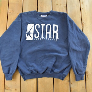 Peut inclure: Un sweat-shirt bleu marine avec l'inscription blanche "STAR LABORATORIES" imprimée sur le devant. Le design comprend une étoile stylisée. Le sweat-shirt est en matière douce et a un col rond.