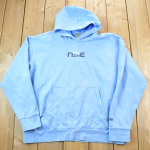 May include: A light blue hooded sweatshirt with a white "NIKE" logo on the front. The sweatshirt has a kangaroo pocket and a drawstring hood.