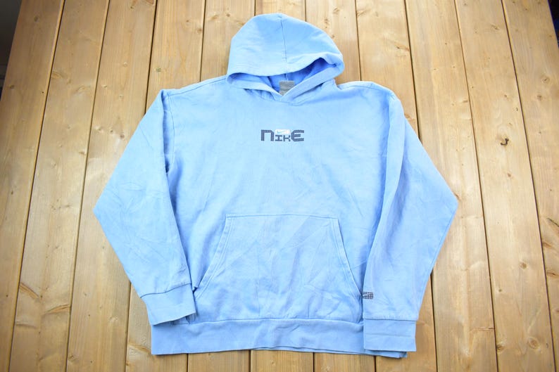 May include: A light blue hooded sweatshirt with a white "NIKE" logo on the front. The sweatshirt has a kangaroo pocket and a drawstring hood.
