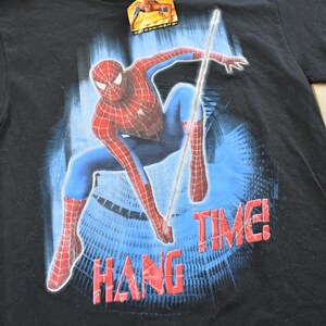 May include: Black t-shirt with a Spider-Man graphic in a dynamic pose, showcasing red and blue costume details. The words "HANG TIME!" are printed in red. A tag is attached at the top.