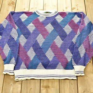 Puede incluir: Un suéter blanco con un patrón de diamantes en tonos de morado, azul y rosa.