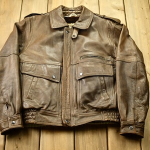 May include: A brown leather bomber jacket with a zipper closure and two large pockets on the front. The jacket has a ribbed knit collar, cuffs, and waistband.