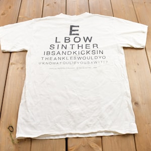 May include: White t-shirt with a black eye chart graphic that reads "E L B O W S I N T H E R I B S A N D K I C K S I N T H E A N K L E S W O U L D Y O U K N O W A F O U L I F Y O U S A W I T I ?"