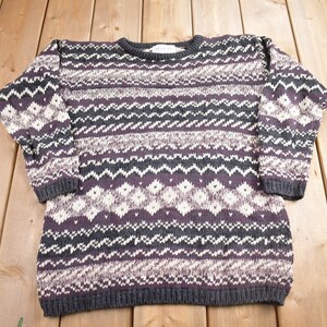 May include: A cream, purple, and black patterned sweater with a crew neck.