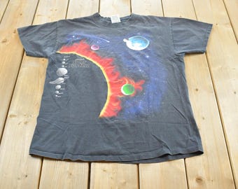 May include: Dark gray t-shirt featuring a colorful solar system design. The graphic includes planets, a red and yellow sun, and the text "Solar System". The shirt has a crew neck and short sleeves.
