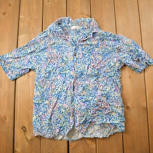 May include: A blue, white and pink patterned short-sleeved button-up shirt with a collar.
