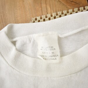 May include: White t-shirt with a white tag that reads "60% Cotton 40% Polyester Youth 8 - 10 Made in Jamaica All Materials"