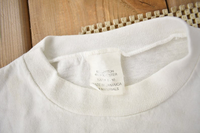 May include: White t-shirt with a white tag that reads "60% Cotton 40% Polyester Youth 8 - 10 Made in Jamaica All Materials"