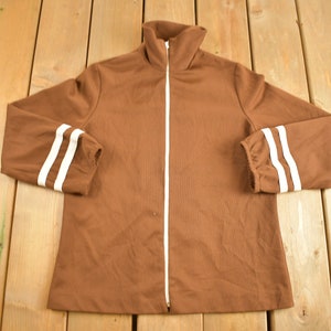 May include: A brown zip-up jacket with white stripes on the sleeves.