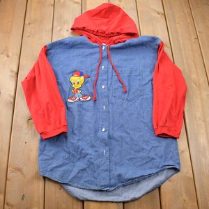 May include: A blue denim button-up shirt with red long sleeves and a red hooded top. The shirt features a cartoon Tweety Bird graphic on the front.