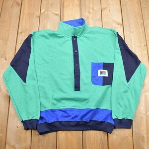 May include: A green, blue and black long-sleeved sweatshirt with a button-up collar and a patch pocket on the front.