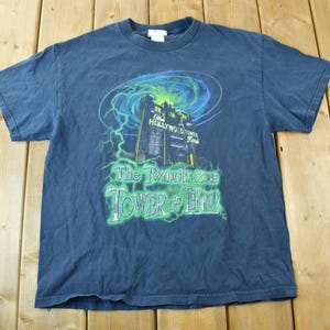 May include: A dark blue t-shirt with a graphic of the Twilight Zone Tower of Terror ride at Disney's Hollywood Studios. The graphic features a green and blue swirling vortex with lightning bolts and the text "The Twilight Zone Tower of Terror".