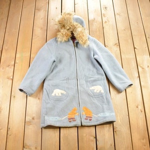 以下が含まれることがあります： フードにファーのトリムが付いたライトブルーのフード付き冬用コート。コートは前面にポケットが2つあり、刺繍されたホッキョクグマとイッカクで飾られています。