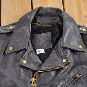 May include: A black leather motorcycle jacket with a zipper closure and gold-toned hardware. The jacket has a fur-lined collar and a label on the inside.